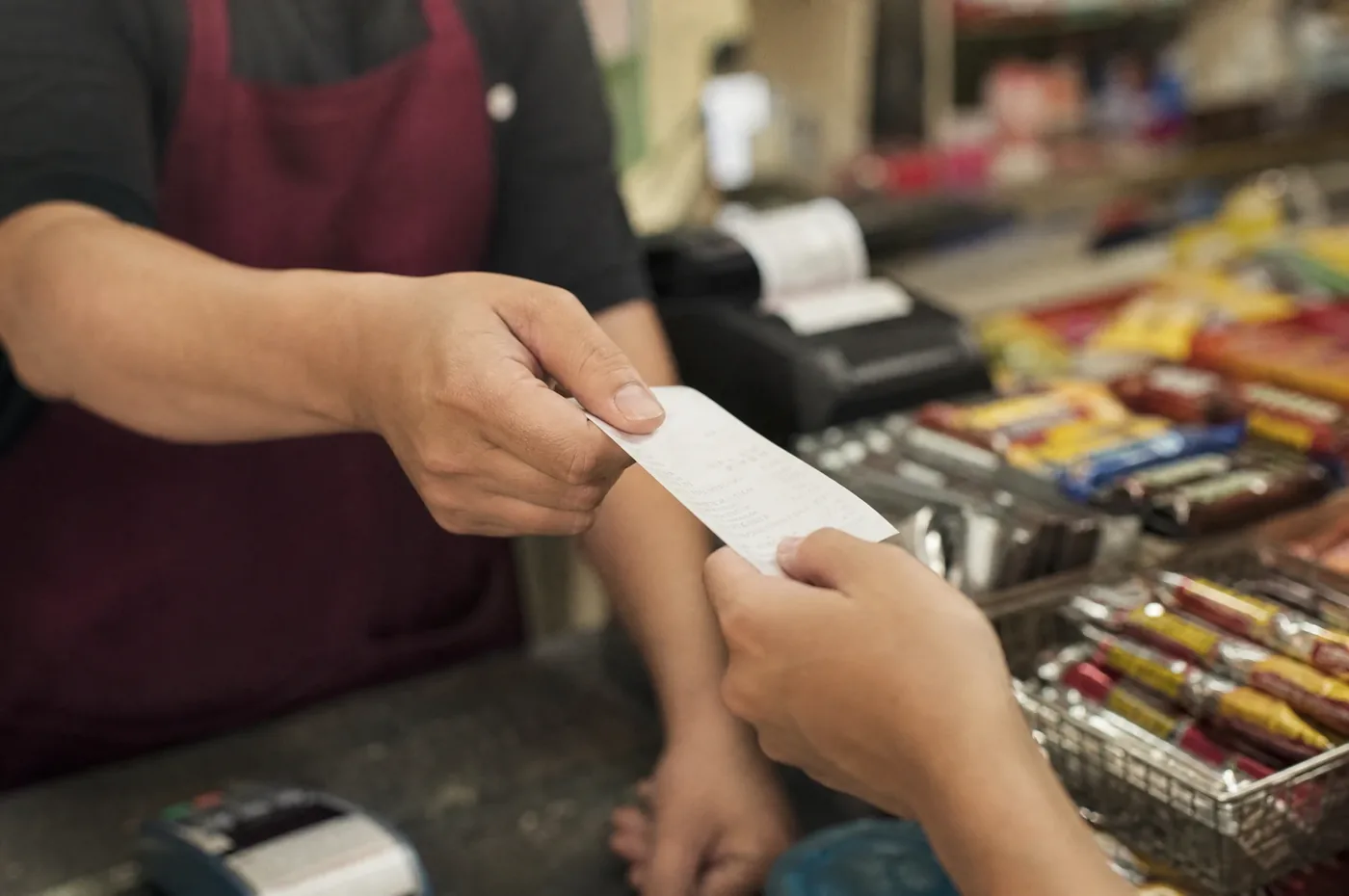 Juruwang menghulurkan resit yang baru dicetak di kaunter kedai runcit