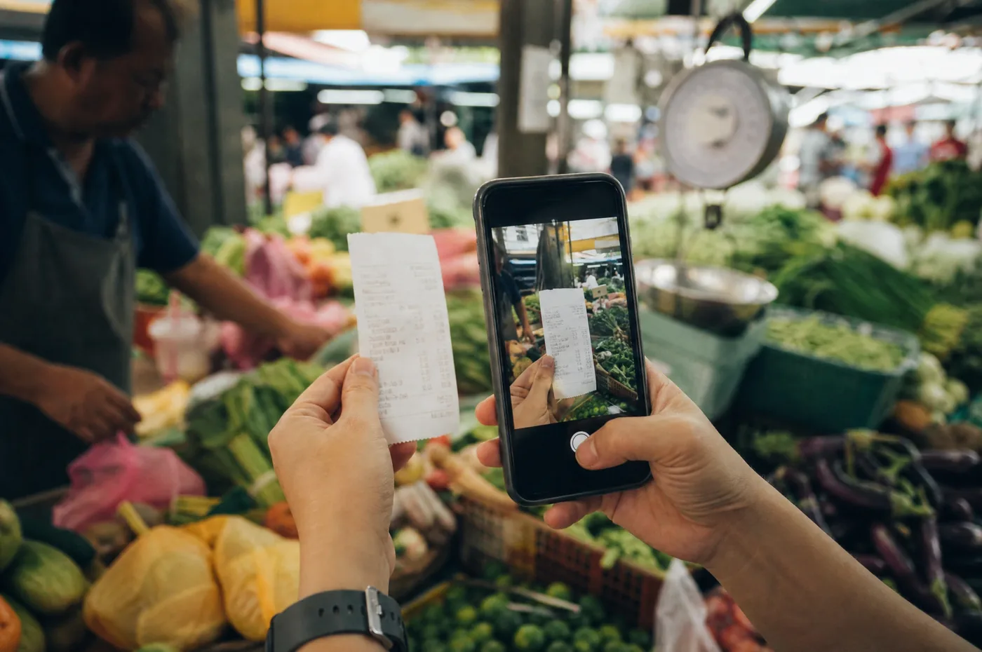 Hands photographing a fresh receipt with an iPhone at a wet market stall
