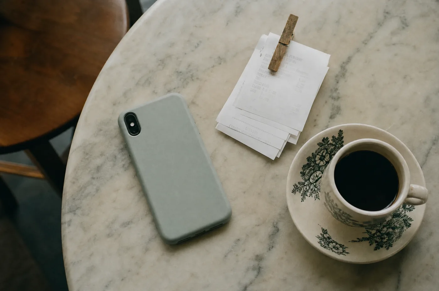 A phone lying face down beside a clipped stack of receipts and a cup of kopi