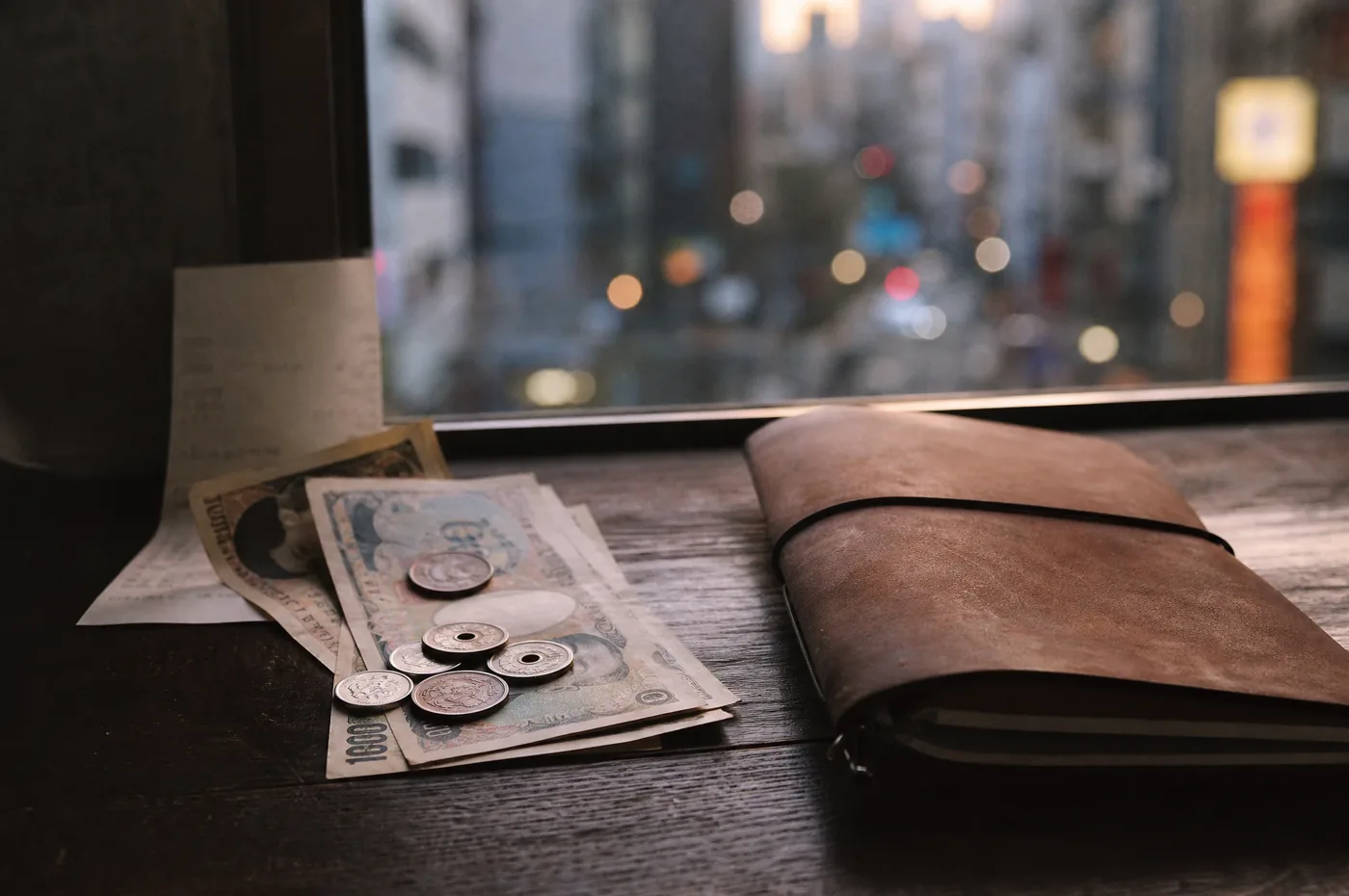 Japanese yen notes and coins beside a folded receipt and a travel notebook, city lights outside